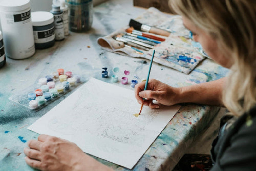 Andrea Mueller painting on a canvas in an art studio with various art supplies around.